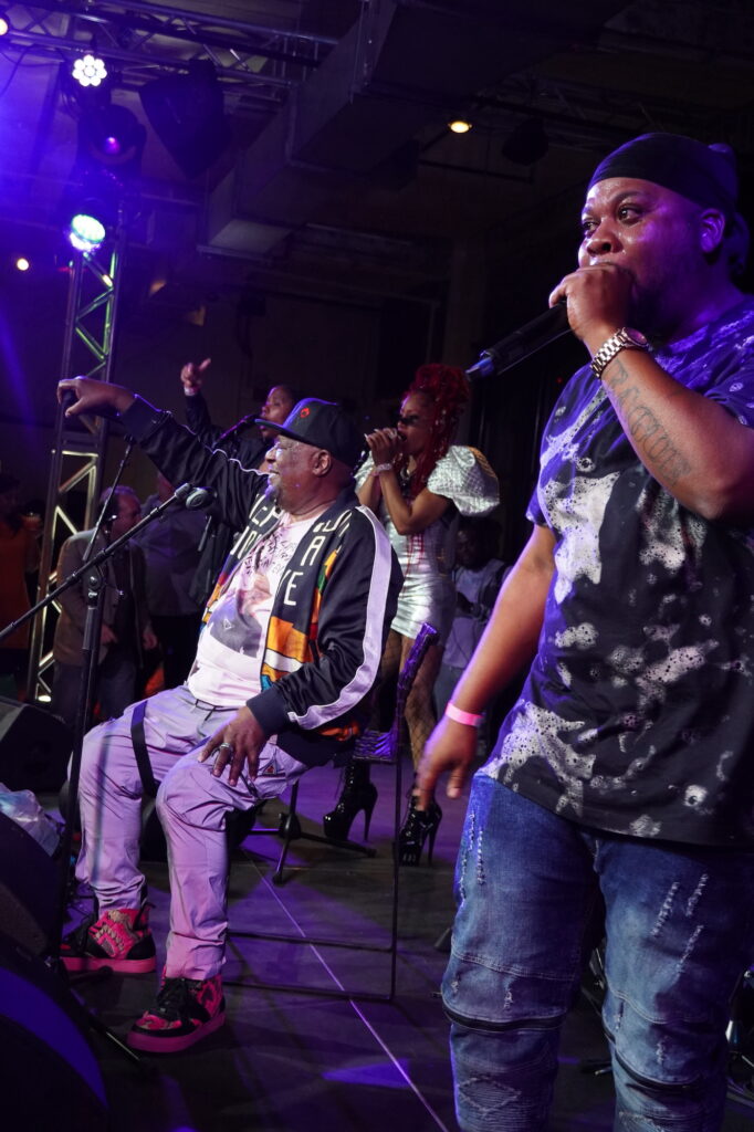 George Clinton sits front and center on a stage, with Tonysha Nelson, Scottie Clinton and Thurteen standing up on both sides of him