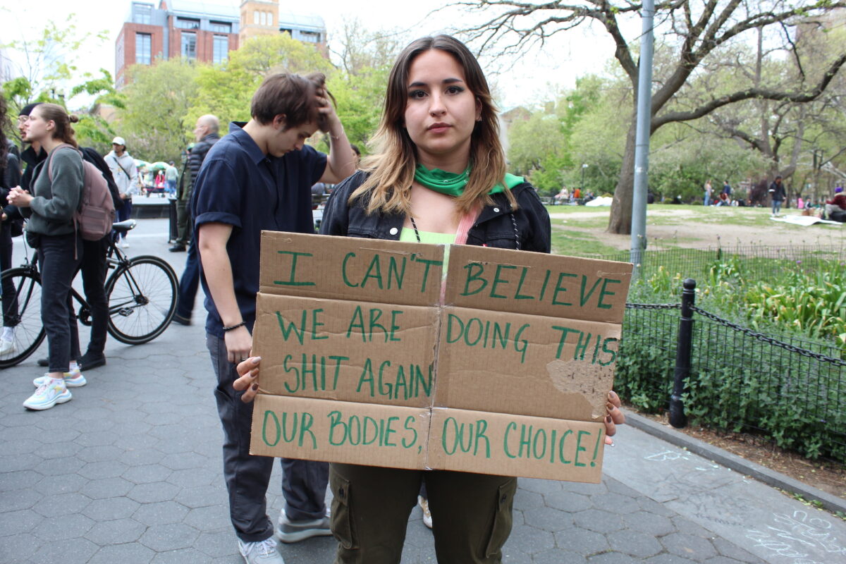 A woman holds up a sign reading “I can’t believe we are doing this shit again. Our bodies, our choice”