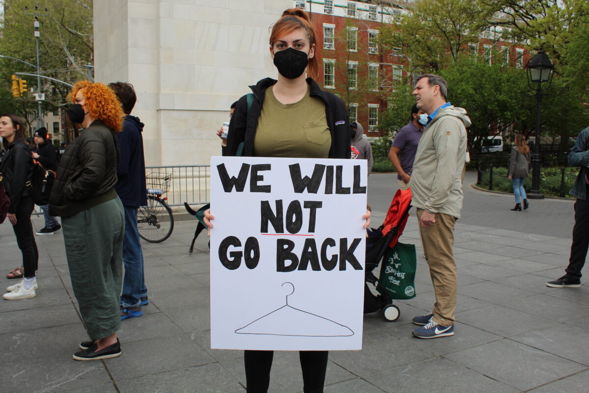 A woman  holds up a poster reading “We will not go back” above a drawing of a coat hanger.