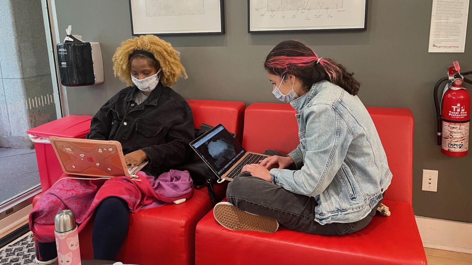 Students wear masks as they sit on couches and work on their laptops