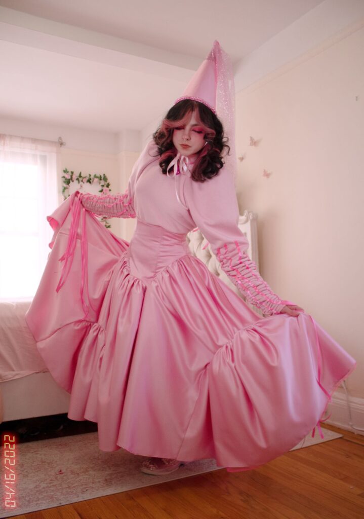 a model wears a pink princess dress with a cone hat