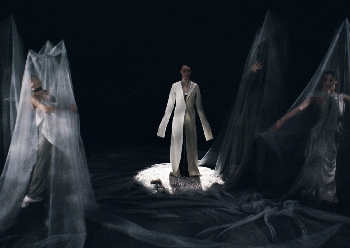 photograph of models in dark room, some covered in sheer blue-gray material