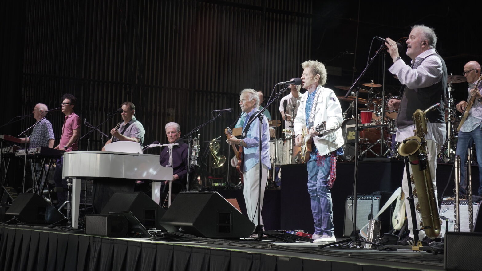 Brian Wilson sitting at a piano onstage on a stage with Al Jardine and Blondie Chaplin, who are singing.