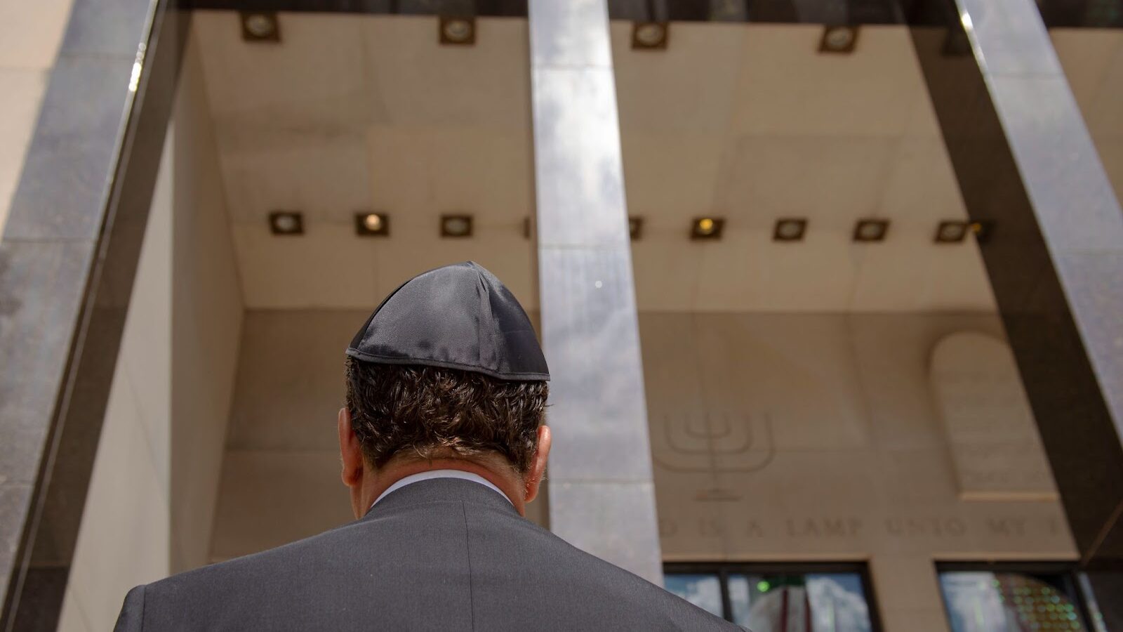 A man in a yarlmulke stands with his back towards the camera while facing the entrance of a building.