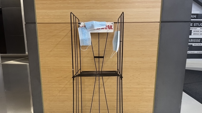 Three disposable masks placed randomly on top of black metal structure in front of wooden-panel at the University Center.