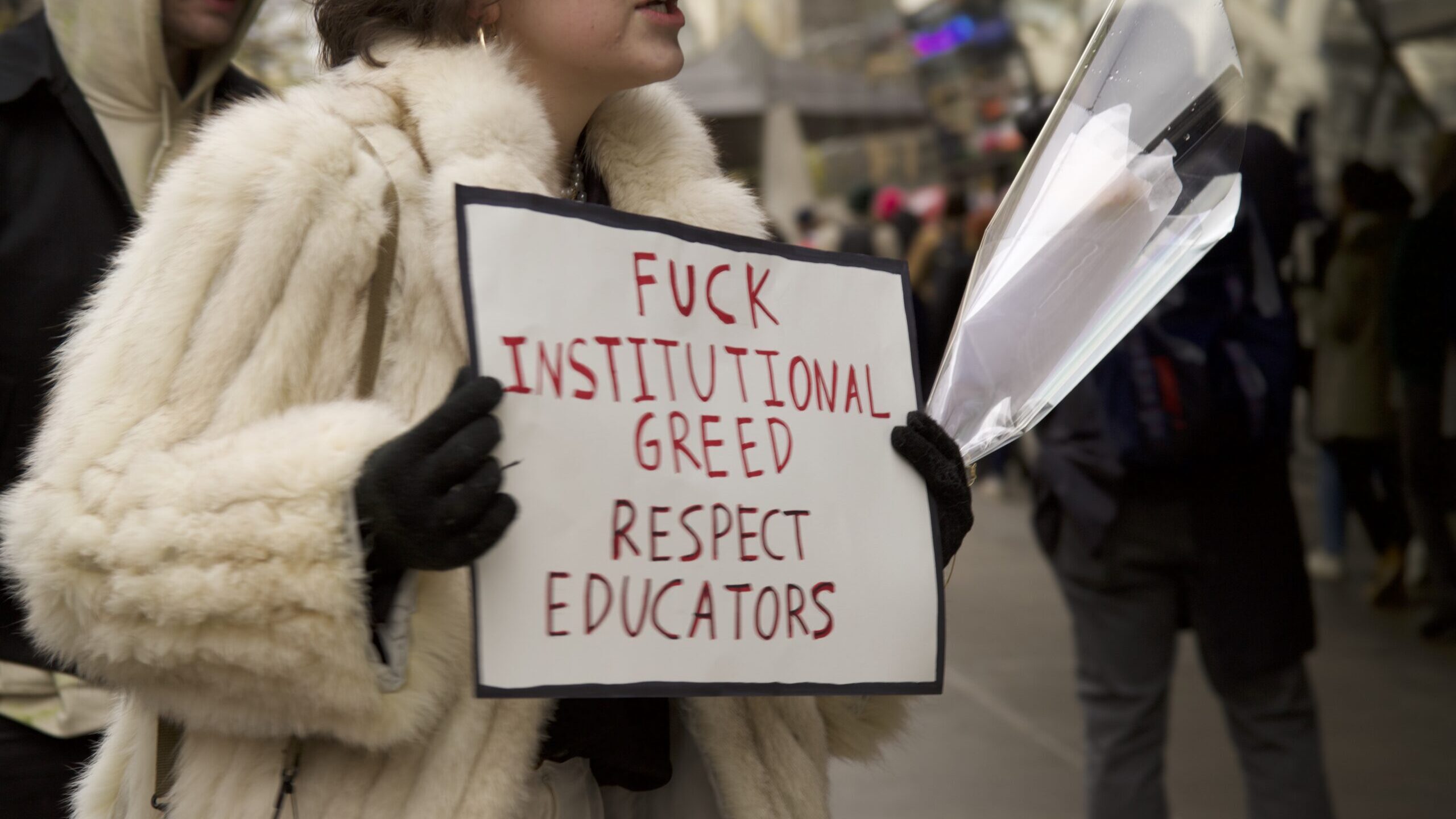 Student at part time faculty strike holding a sign stating "fuck institutional greed, respect educators"
