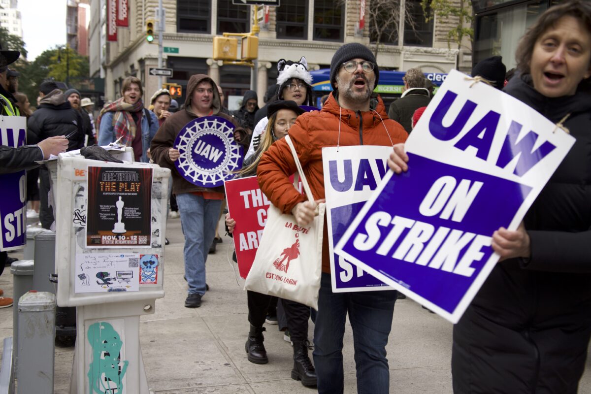 Protesters outside The New School holding signs. A sign in blue and white reads "UAW ON STRIKE" 