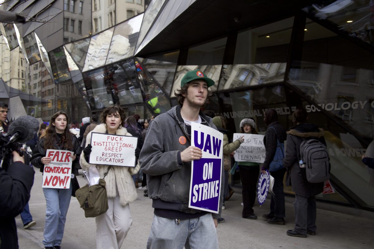  Three protesters are depicted outside of The New School with signs that read one blue sign ‘UAW on Strike” a red handwritten sign that reads “Fuck Institutional Greed Respect Educators” and a red handwritten sign that reads “Fair Contract Now”