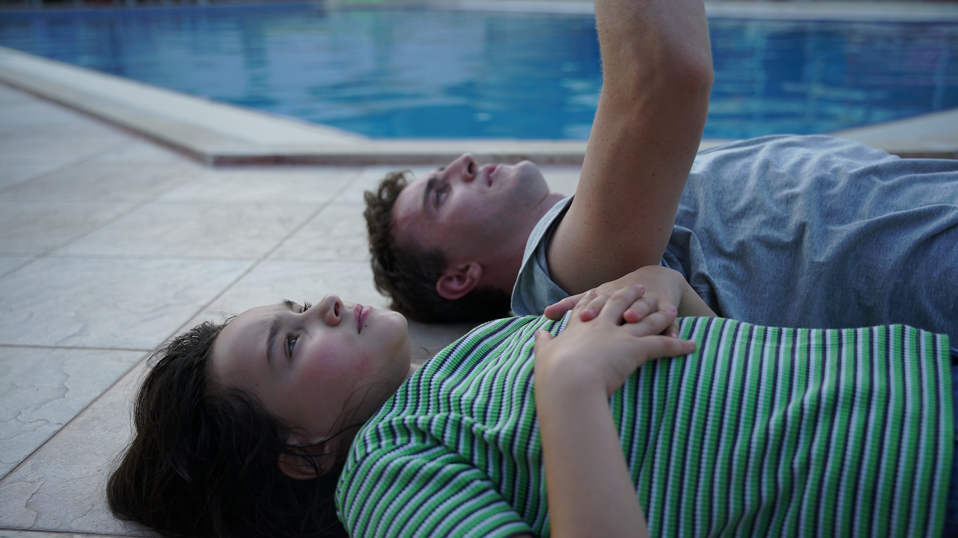 Calum and Sophie in movie Aftersun lay poolside staring at sky