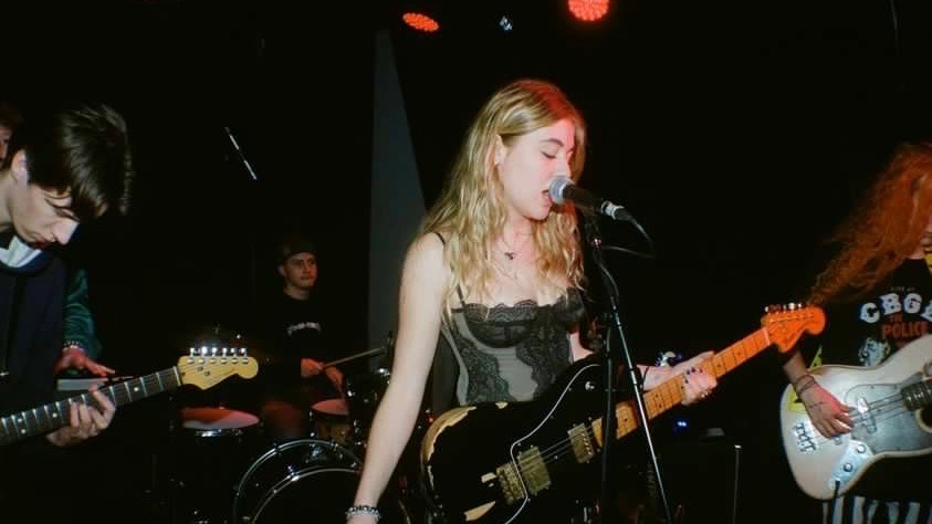 True Jackson stands on stage in a black tank top, playing a black electric guitar