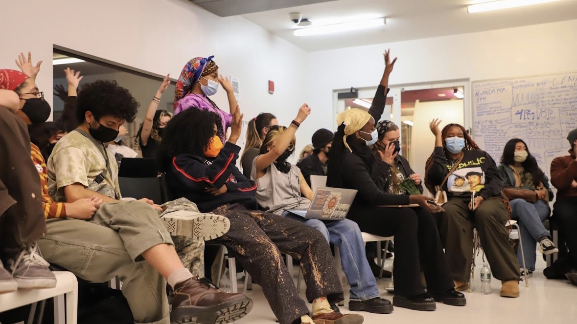 Students sit together in the University Center event cafe. Some students raise their hands and others listen attentively.