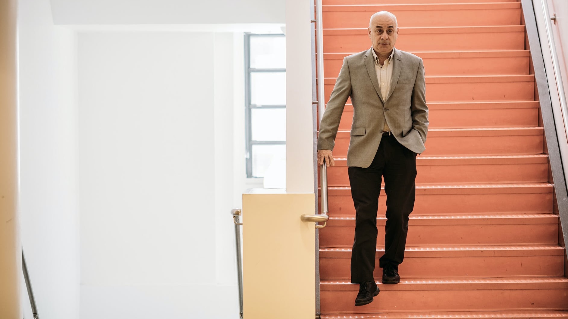 Image of William Milberg, current dean of NSSR, walking down red stairs in the NSSR building which is located at 6 E. 16th St.