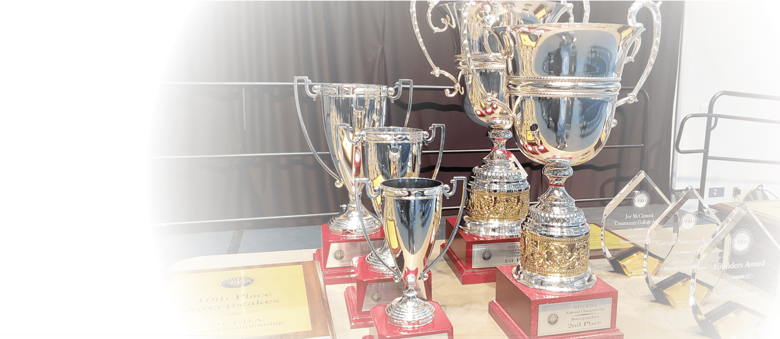 A plaque, five silver CEDA National Championship trophies, and three glass awards set on a table