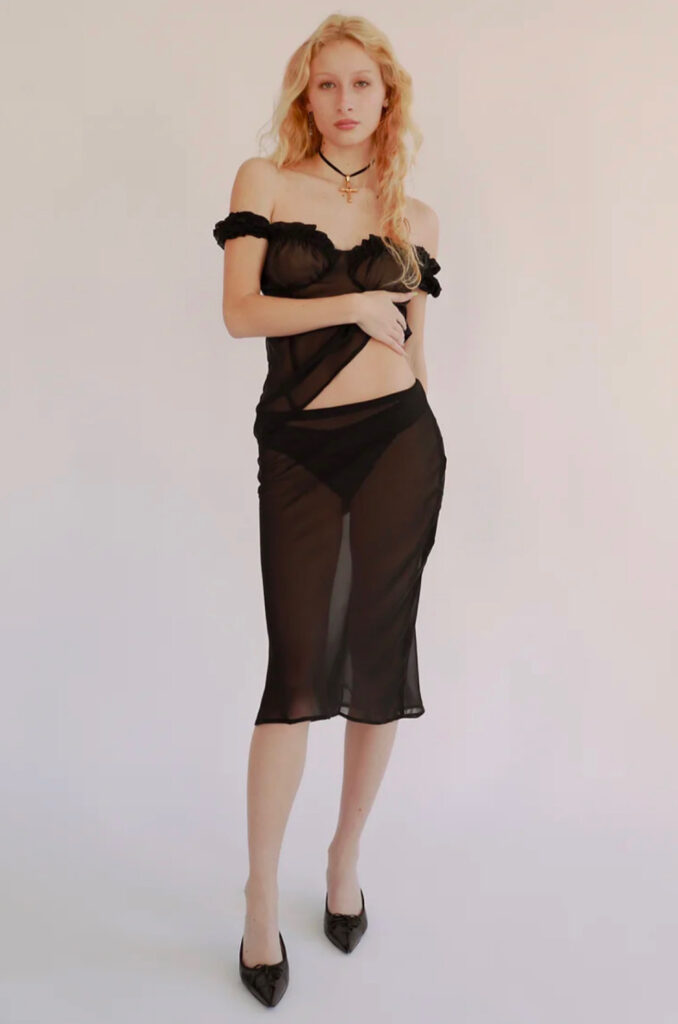 Blonde haired girl pictured in front of blank background in black skirt, shirt and shoes