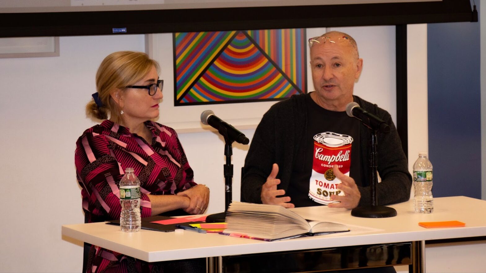 Fenton Bailey and Liesl Schillinger, sitting at a table talking with a large projector behind them..