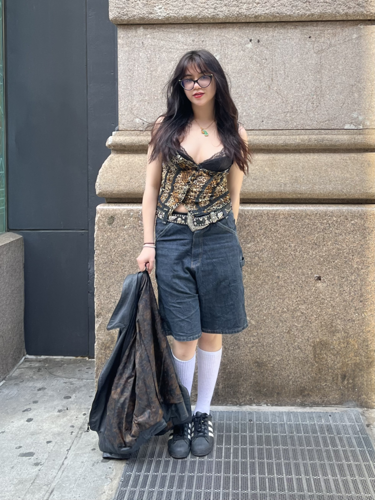 First-year drama student wears a leopard print tank top, a bedazzled belt, jean shorts, and Adidas sambas while posing on Fifth Avenue.