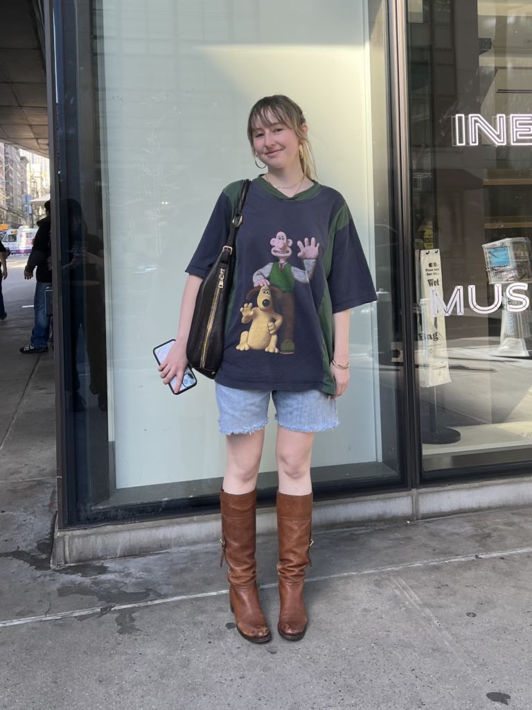 Third-year fashion design student wears brown boots, jean shorts, a Prada bag, and a Wallace and Gromit t-shirt.