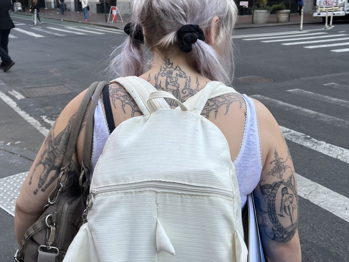 Student wears a white backpack on top of tattoos that cover her neck, back, and arms.