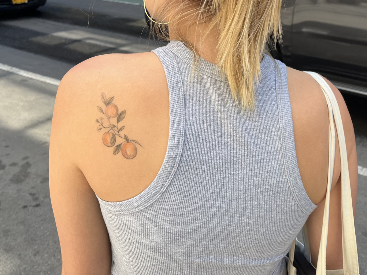 Student faces away from the camera wearing a gray tank top to reveal a tattoo of three clementines on her shoulder blade.