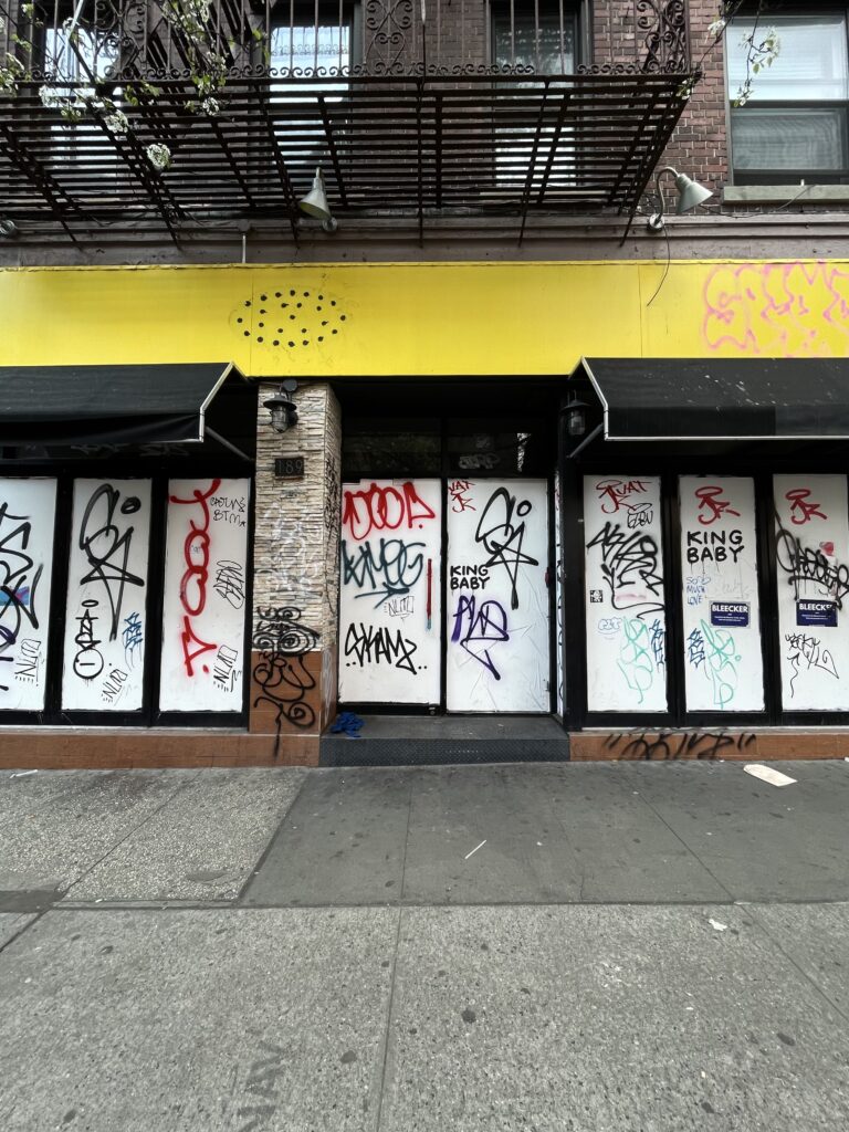 A series of white windows covered in red, black, blue, and green graffiti underneath a neon yellow boarder and a fire escape above. 