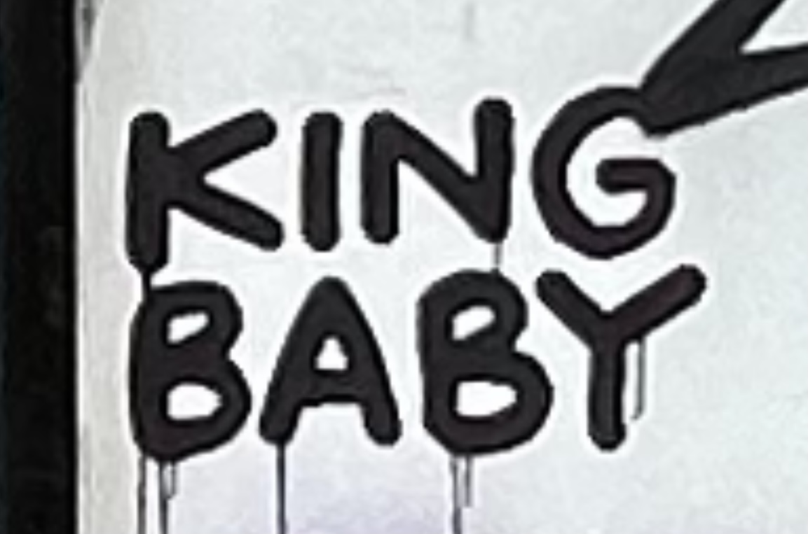 "King Baby" spray painted in black on a white wall. 
