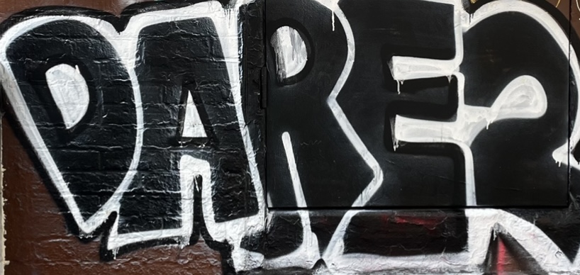 "Darer" spray painted in big black and white bubble letters on a brick wall. 