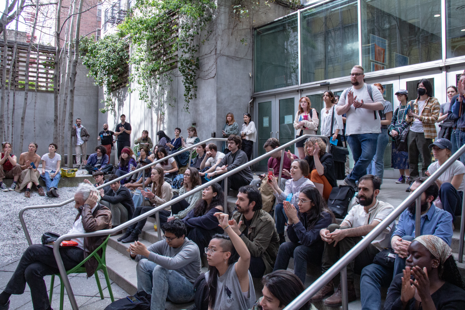 image of people gathered on the steps of a courtyard. They are clapping and a person holds a fist up in the air.