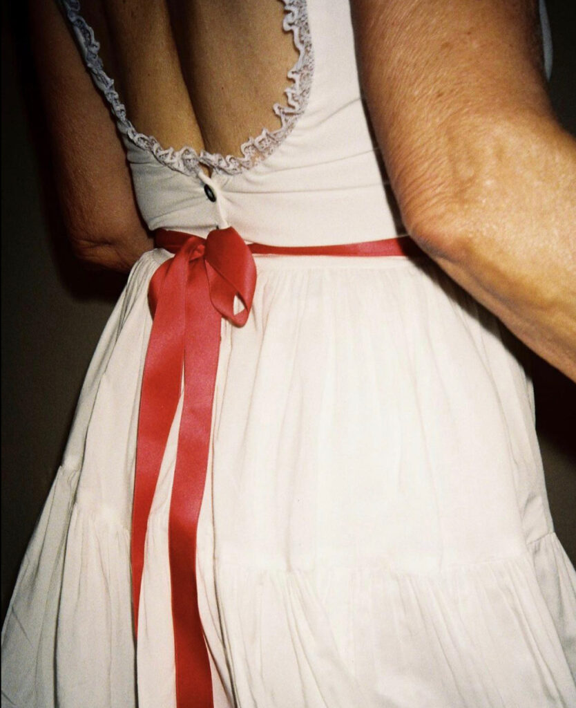 Womans back in a white dress with lace details and a red ribbon