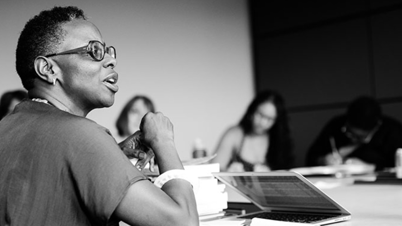 Thompson is at the left of the image speaking to blurred individuals visible behind her, classroom setting (in black and white).