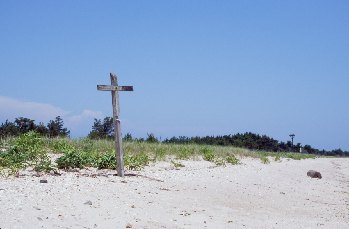 Photograph of a cross sticking out of the sands on a beach