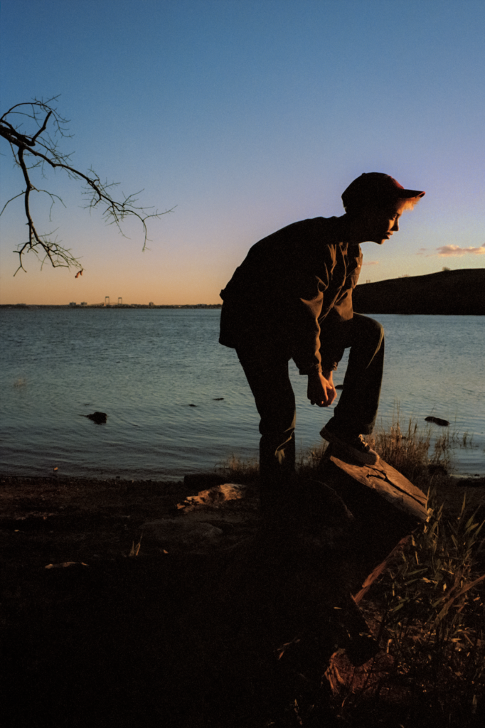 Photograph of a person standing on a rock next to a lake at dusk