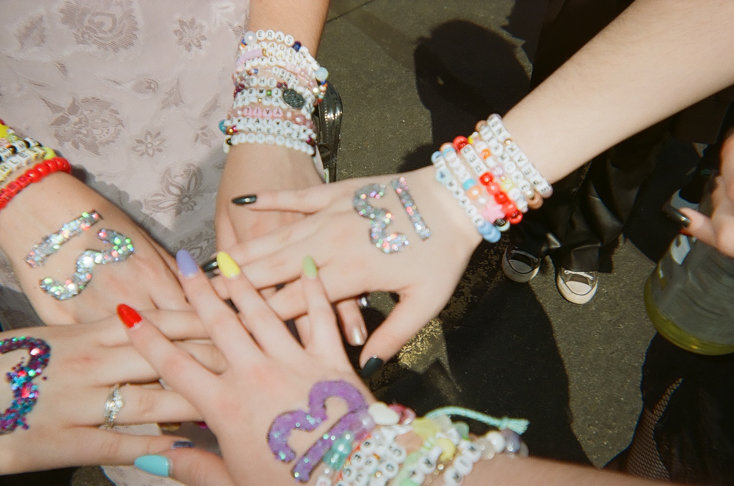 Four hands placed together with number 13s drawn on their hands and friendship bracelets on their arms.