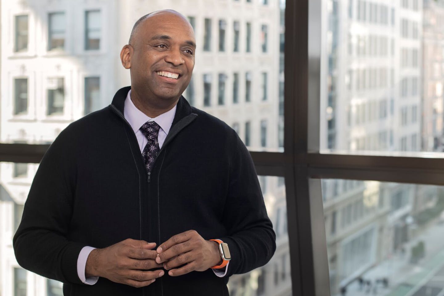 President McBride smiling, wearing a black sweater over shirt and tie, with the New York City skyline behind him.