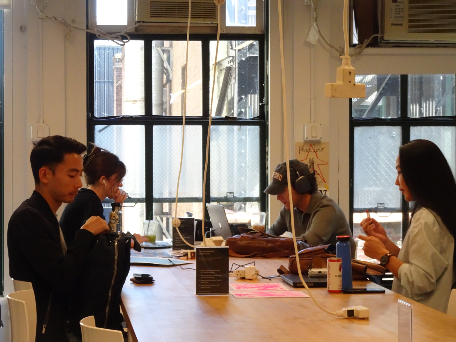 Four students sitting around a wooden table in the Design Lab at the 2 West 13th Street Parsons building. Two students farthest from the camera are working on their computers. Photo by Remy Grimm