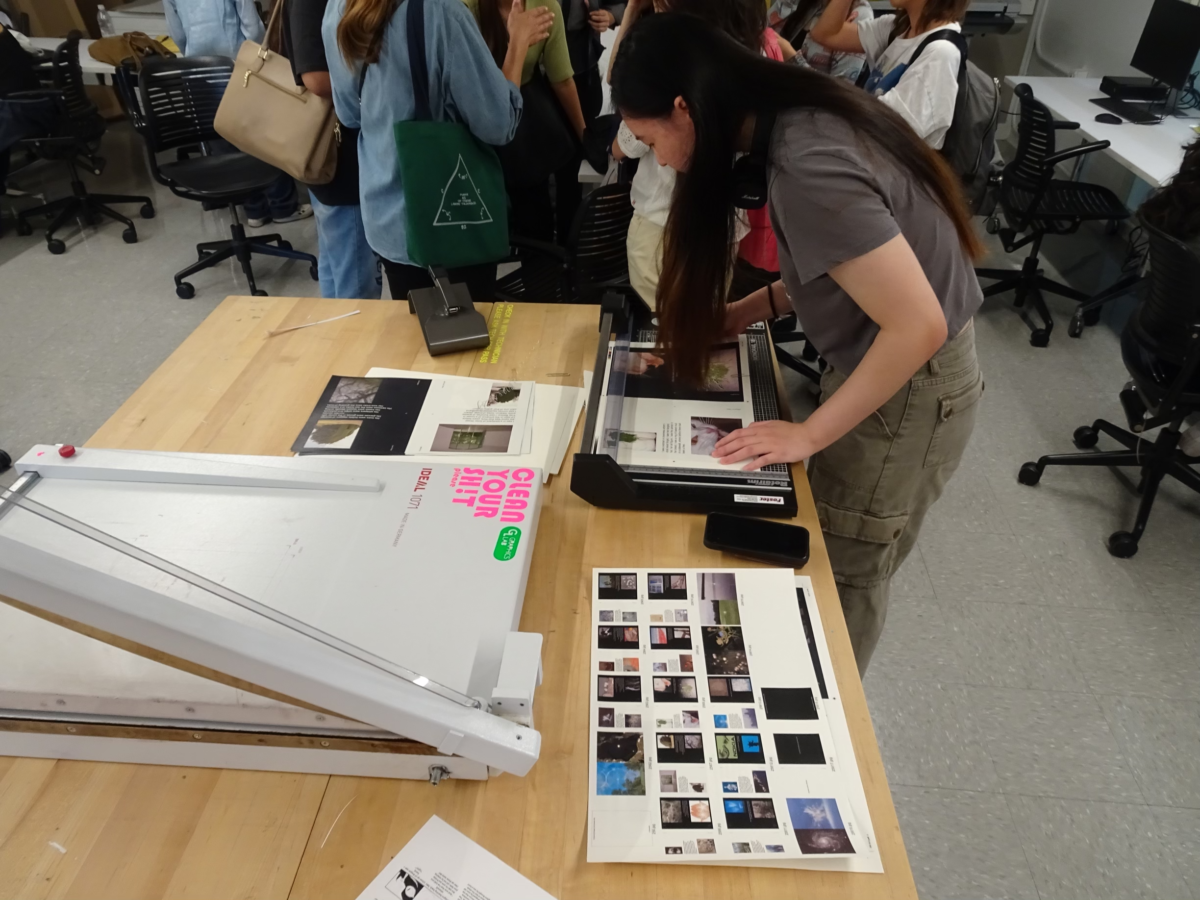 Student in a grey shirt and green pants leaning over a paper guillotine cutting prints in the Design Lab at Parsons. Photo by Remy Grimm