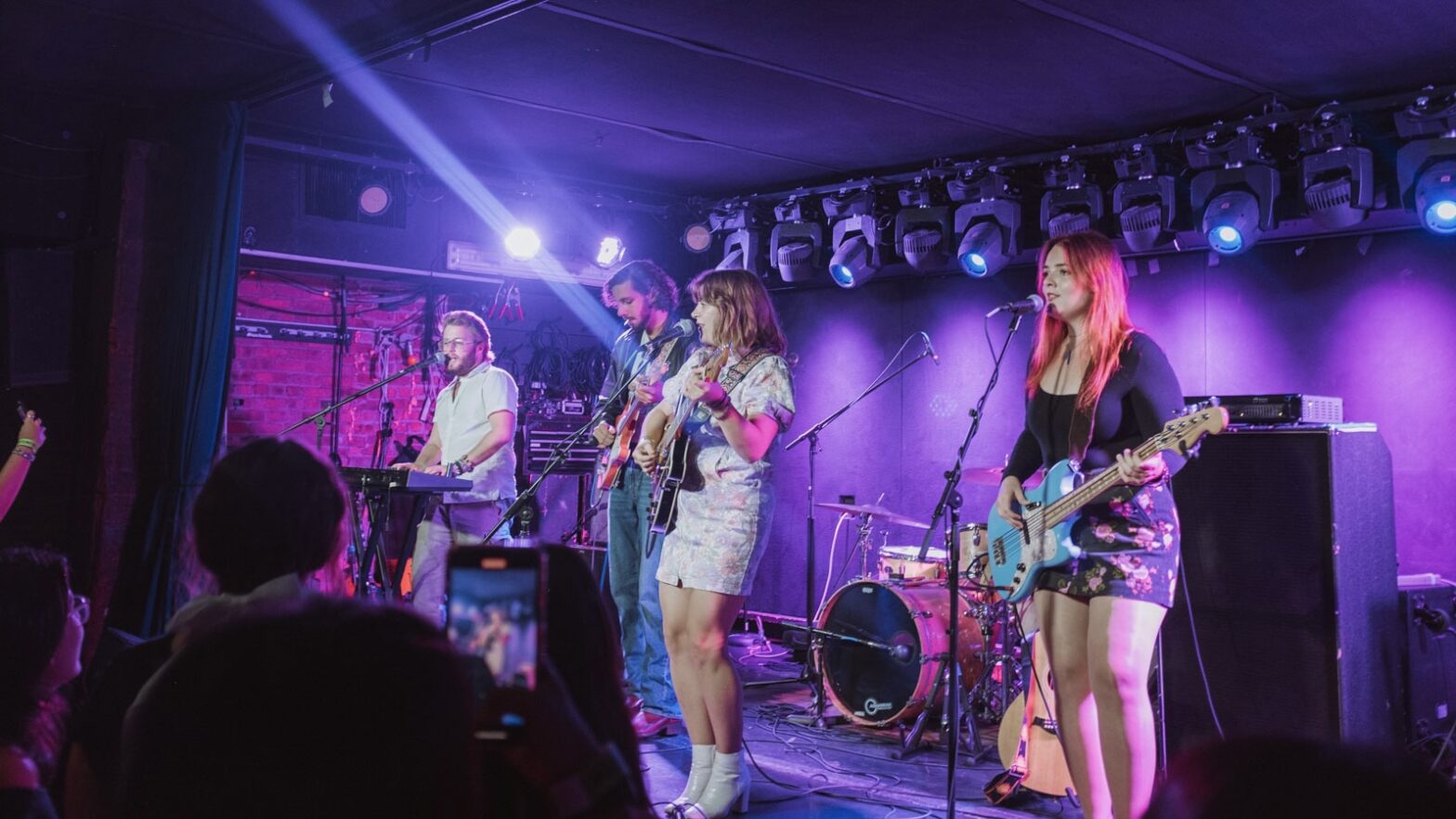 Sarah Gross and three band members performing on a stage colored with pink and purple lights.