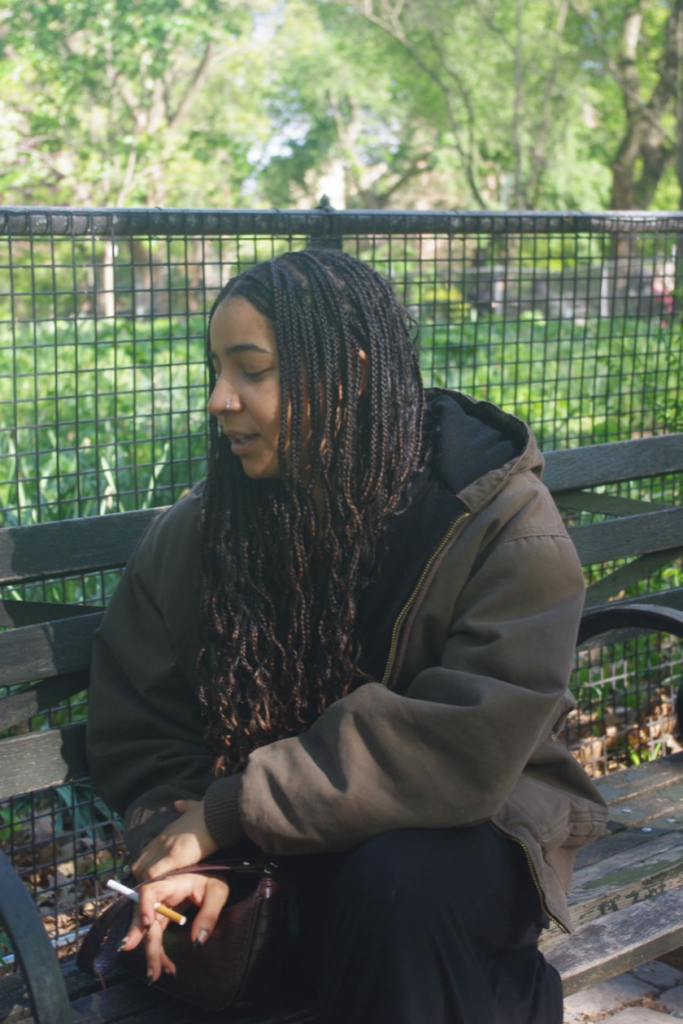 Girl sitting on a park bench while smoking a cigarette.