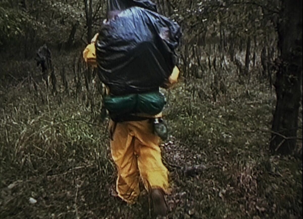 A screen capture from “The Blair Witch Project” that shows A hiker in rain gear in a forest.