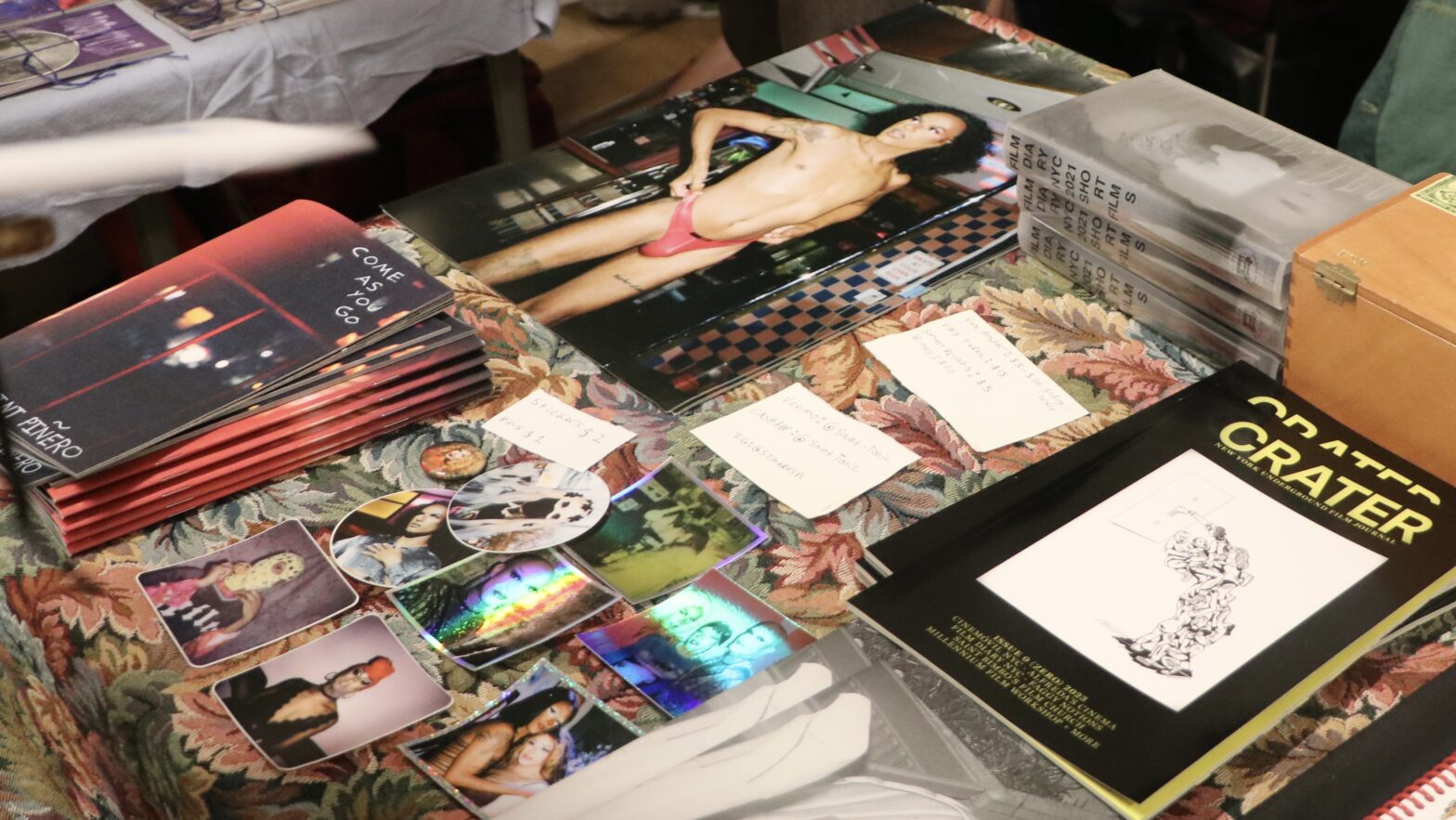 Zines, stickers, booklets, and posters stacked on a floral print display table.