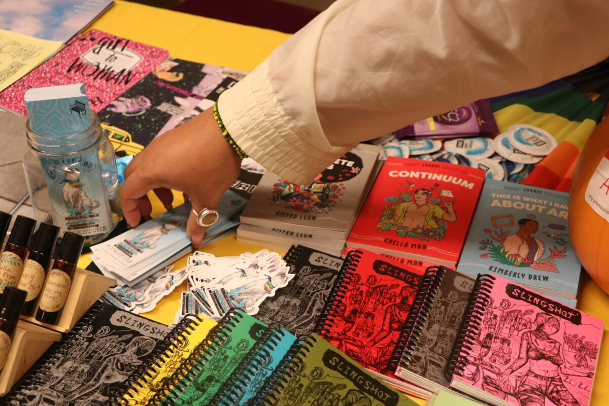 Hand reaches over table filled with zines