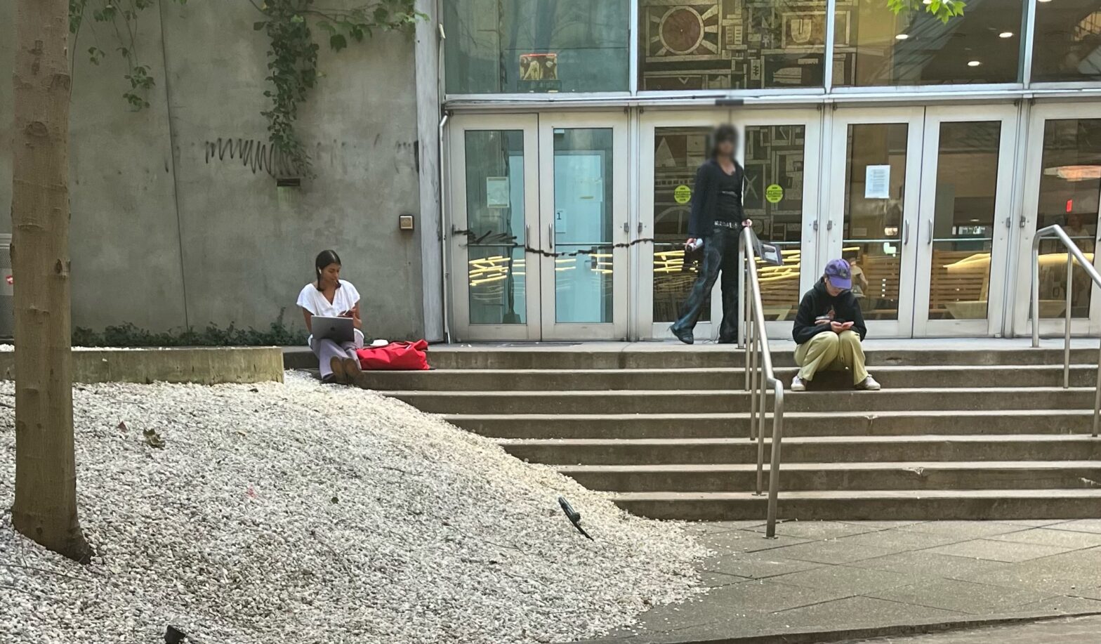 A student holding a computer and spray paint in a courtyard