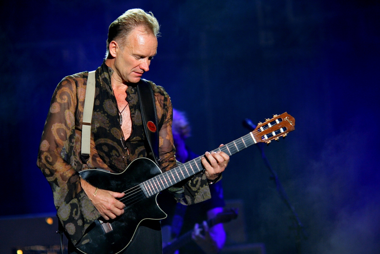 singer Sting holding a black guitar on a stage