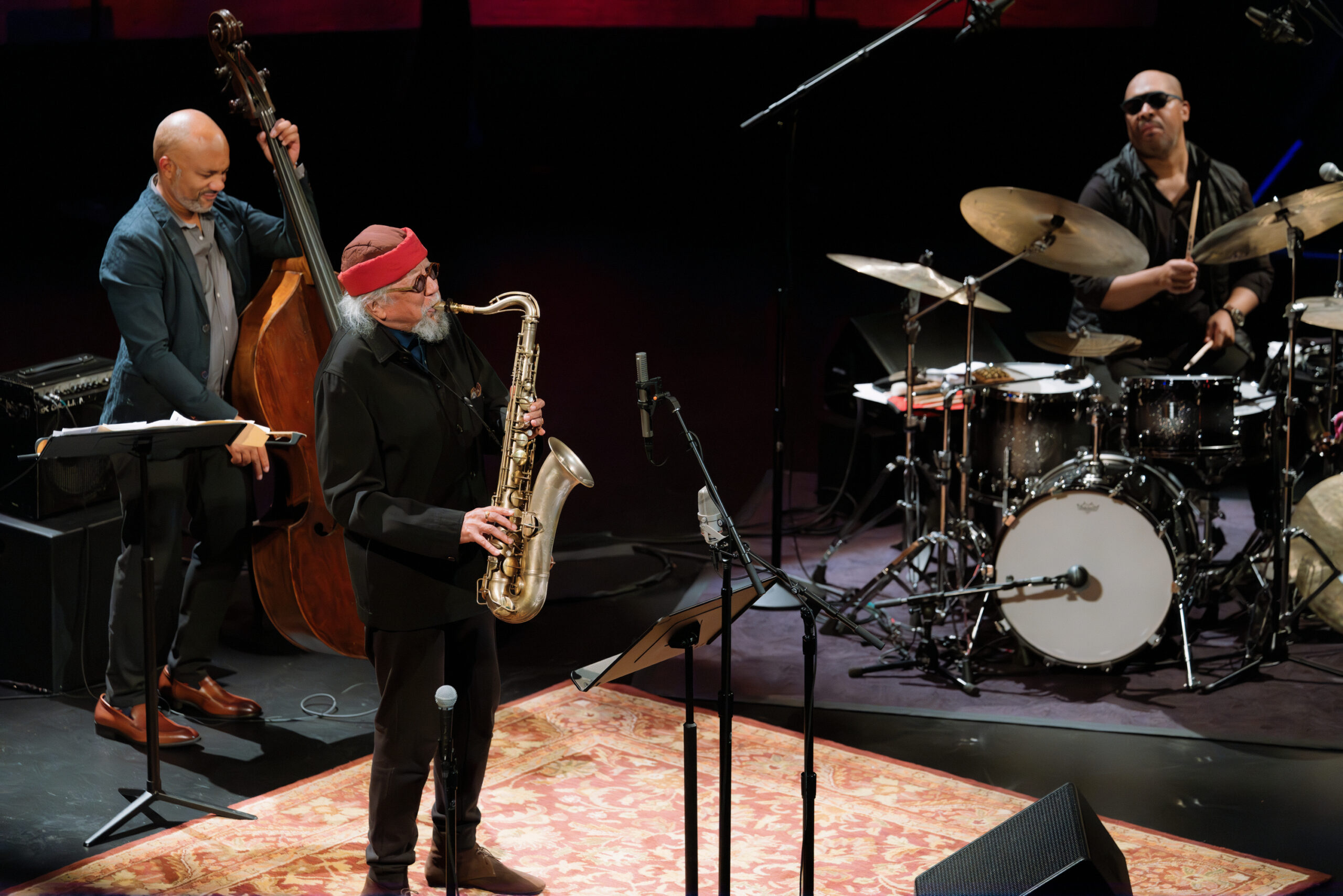 Three men onstage playing saxophone, bass and drums.