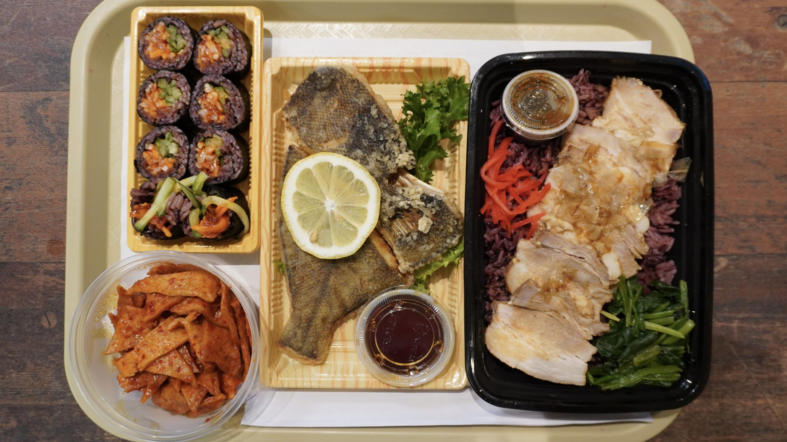 A tray with boxes of fish, Kimbap, Pork and rice cakes.