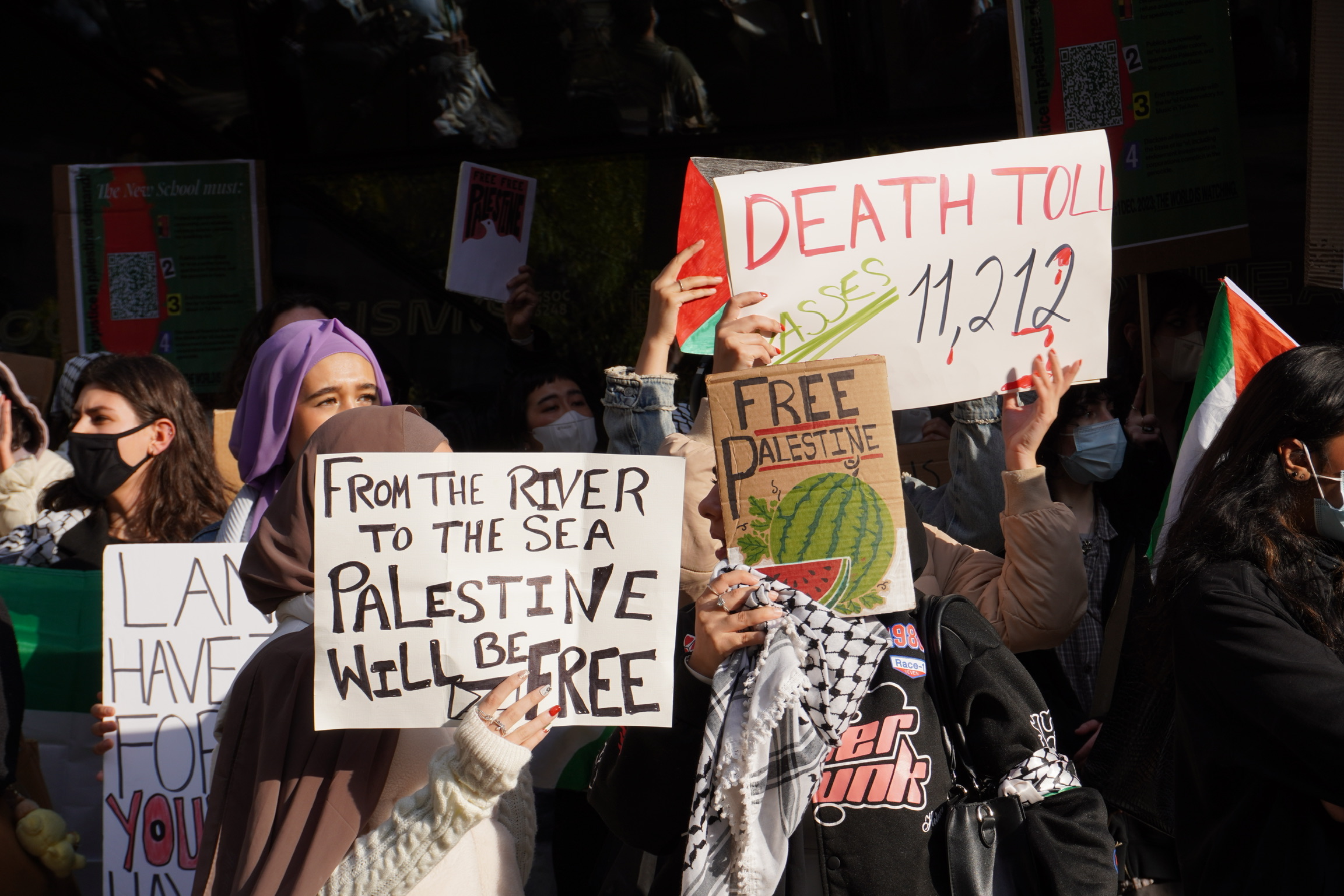 New School community members pictured at the walkout outside of the University Center at 63 Fifth Ave, holding up multiple signs that read “From the river to the sea Palestine will be free,” “Death toll passes 11,212,” and “Free Palestine.”