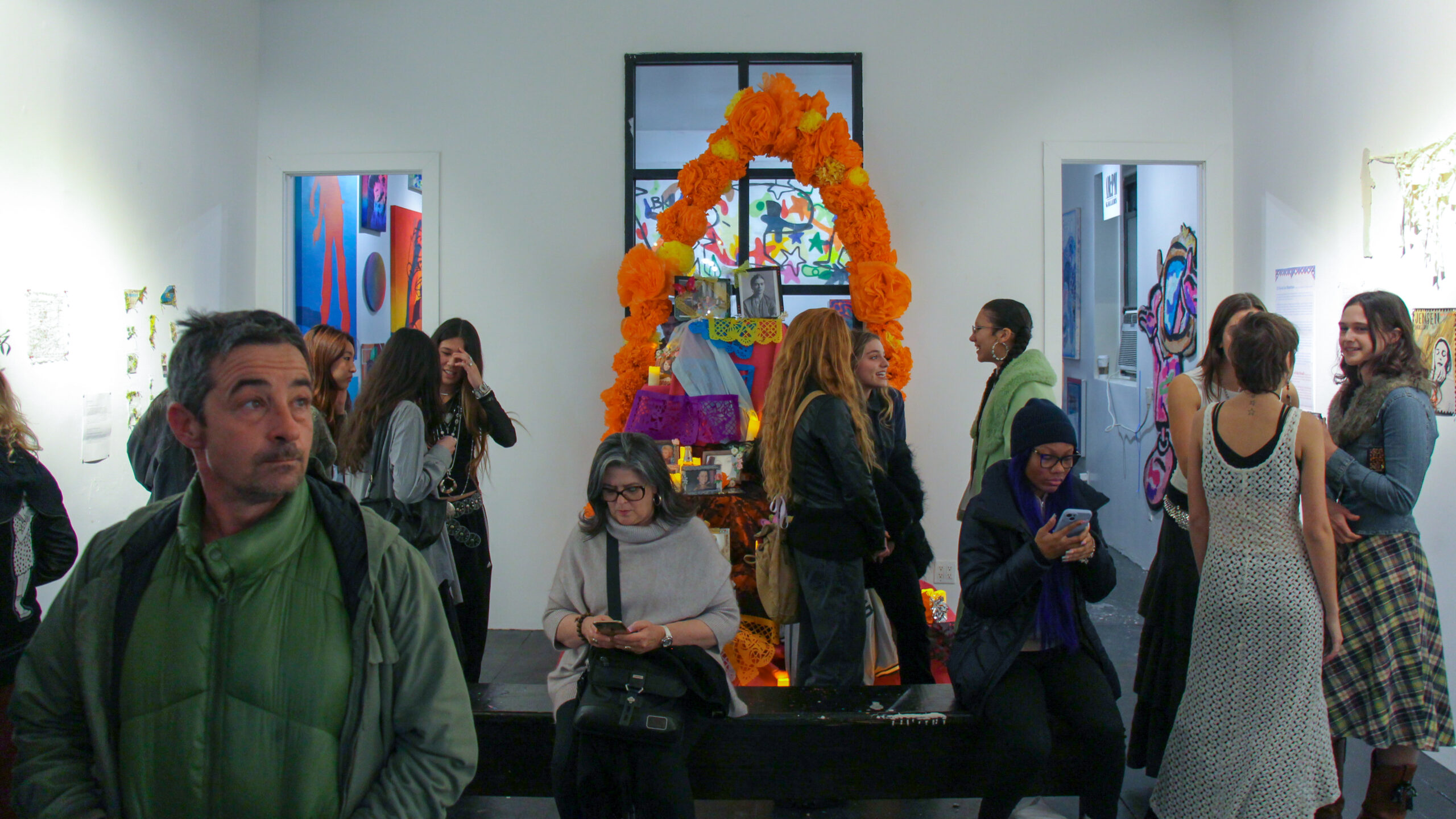 People stand talking in a gallery room with a colorful altar in the middle.