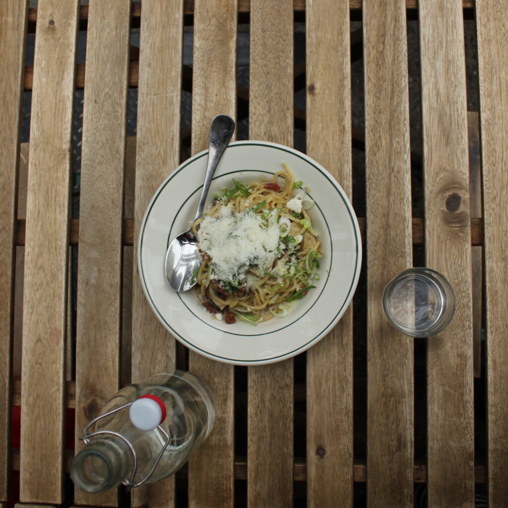 Carbonara is served on a wooden table next to a glass of water.
