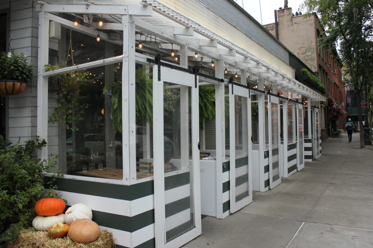 A row of outdoor booths on the sidewalk with lights and plants.