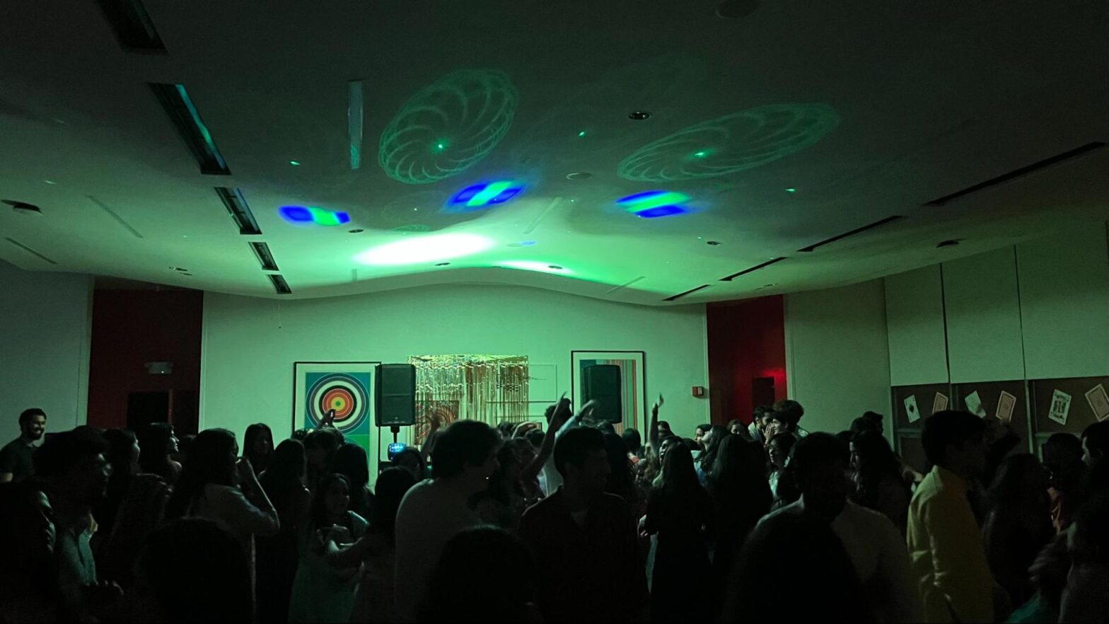 Green and blue lights flash on the ceiling at Wollman Hall over a silhouetted crowd of people.