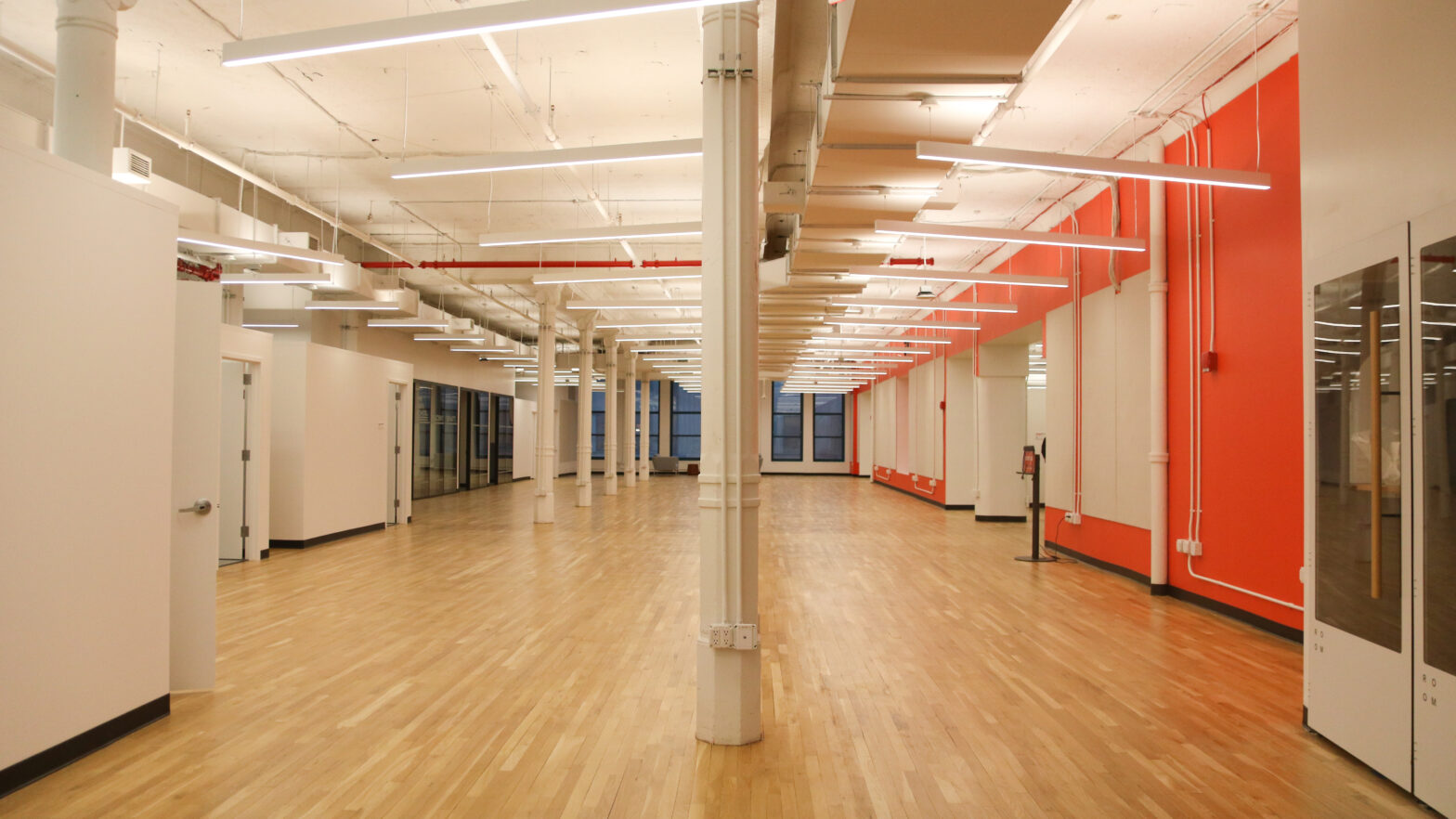 Open empty room with white walls, beams, and an red accent wall.